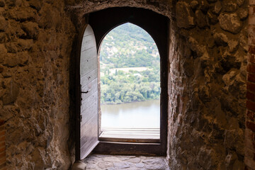 Old wooden door opening into nothingness in a historic castle on a mountaintop, with a river and forest landscape in the distance