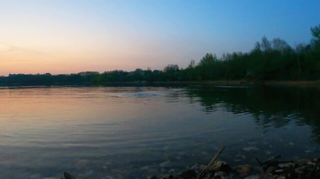 Throwing stones in calm lake making splashes and ripples at sunset surrounded by serene natural landscape