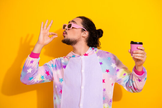 Young man in pastel star pajama with pink sunglass holds coffee on bright yellow background