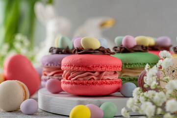 Easter macarons decorated with a chocolate nest and egg-shaped candies on top on a marble board on concrete background. A cute Easter dessert. Copy space.