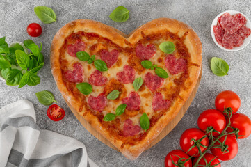 Heart shaped Italian pizza with salami, cheese and fresh basil on a concrete background. Holiday concept for Valentine's day. Top view. Copy space