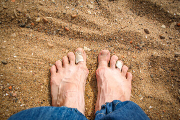 bare feet standing on sand, symbolizing a raw and personal journey. Toes wrapped in medical bandages after difficult travels or long walks. For themes of endurance, exploring the world on foot
