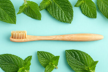 Bamboo toothbrush placed on a soft blue background surrounded by fresh mint leaves, emphasizing eco-friendly dental care and natural hygiene solutions