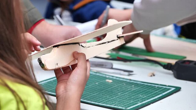 Hands assembling balsa wood airplane model during DIY craft workshop