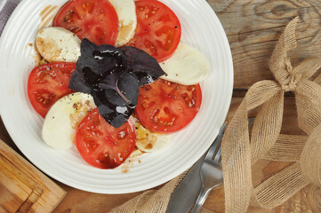 Caprese salad - tomatoes, basil and mozzarella cheese on a wooden background