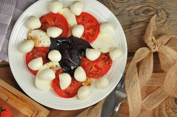 Caprese salad - tomatoes, basil and mozzarella cheese on a wooden background
