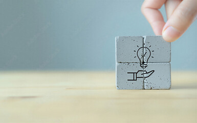 Hand holding stacked concrete blocks with light bulb idea on table top