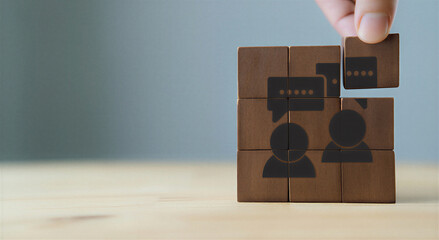 Hand holding wooden puzzle piece with chat and people icons on table