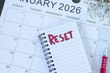 Reset handwritten word in notebook with January 2026 calendar. Top view. The concept of change, new...