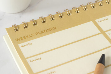 Weekly planner with daily notes and to do list blank page with coffee cup on white marble background. Close-up. Personal resolutions, aspirations, goals, and time management concept.