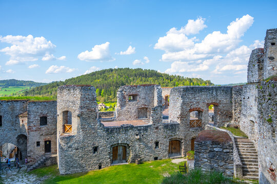 Visitors stroll through the courtyard of Rabi Castle, surrounded by ancient stone walls and lush green hills under a bright blue sky. The historic site offers a glimpse into the past. - Powered by Adobe