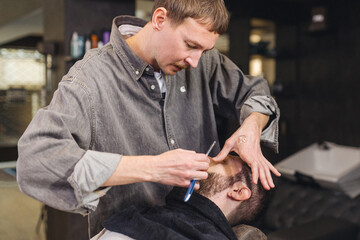 Close up of professional barber shaving male neck with straight razor in barbershop. Beard contouring, classic wet shave, men grooming service and barber work process concept.