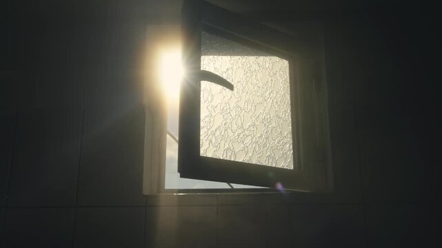 Sunlight penetrates through an bathroom open window  casting relaxing warm ambiance with steam visible suggesting humid shower environment