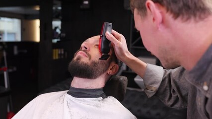 Professional barber trimming client hair with electric clipper in modern barbershop. Male grooming service, precise hairstyling process, focused expression, contemporary salon interior.