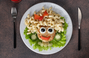 Fun Food for kids - smiling face girl from turkey cutlet, pasta cavatappi, olives, pepper, egg and cucumber on white plate, Top view