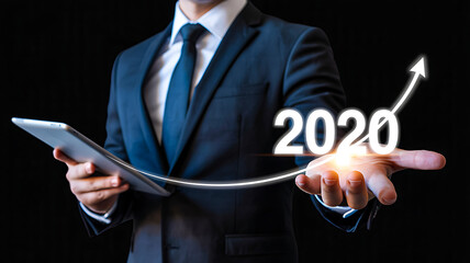 Businessperson holding tablet with glowing “2020” digits above cityscape, symbolizing innovation and new beginnings