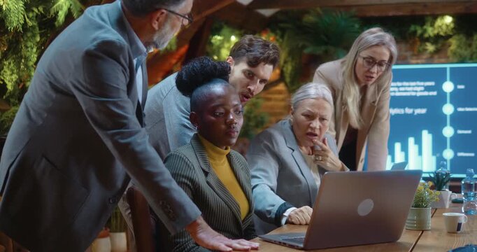 Business team looking at laptop and reacting negatively to bad news during corporate meeting, showing disappointment and concern after loss or market decline in modern eco-friendly office.