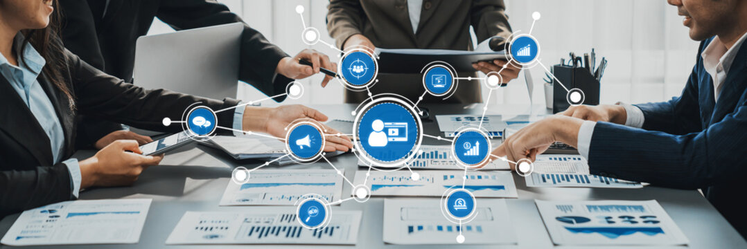 A professional team collaborates on marketing strategies, interacting with digital tools and data charts in a modern office setting, showcasing teamwork and innovative solutions. Amity - Powered by Adobe