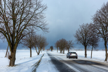 Country road in the winter during the snow blizzard. Road surfece covered with snow and ice. Dangerous car travel condition.