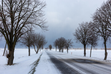 Obraz premium Country road in the winter during the snow blizzard. Road surfece covered with snow and ice. Dangerous car travel condition.