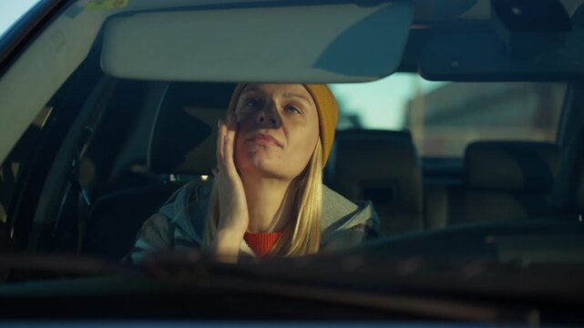 Young woman in car applying moisturizer while check reflection in rearview mirror, then adjusting sun visor to shield face from bright morning sunlight