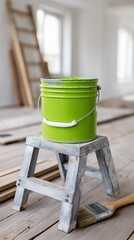 Bright green paint bucket on small wooden ladder in renovation site with drywall and ladder