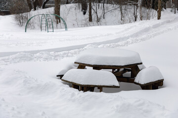 Picnic table covered with snow in park with playground in winter