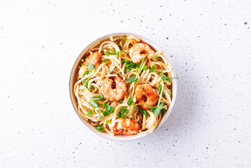 Spaghetti with cream sauce, parmesan, shrimps and onion, decorated with pea micro greens in white ceramic bowl on light stone background top view. 
