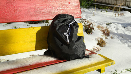 black bag lying on a colored bench in a winter park