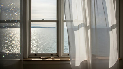 Bright interior view of a window with white curtains blowing in the wind overlooking the ocean