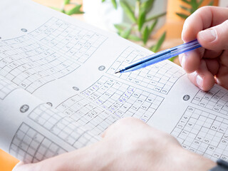 Man holding pen and solving difficult sudoku logical puzzle in paper book at home