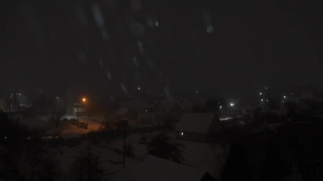Intense snowfall at night. Houses and street lights are visible in the dark Village. View from the window during the storm in Winter