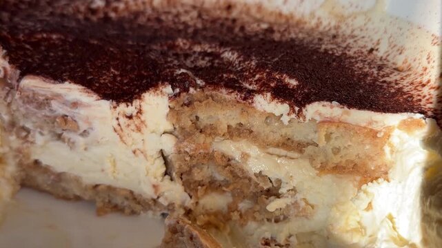 Taking a little piece of traditional classic dessert tiramisu by spoon close-up. Popular Italian sweet tiramisu made of ladyfinger pastries and dipped in coffee, layered with a whipped mixture of eggs