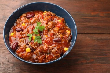 Delicious chili con carne in bowl on wooden table, closeup. Space for text