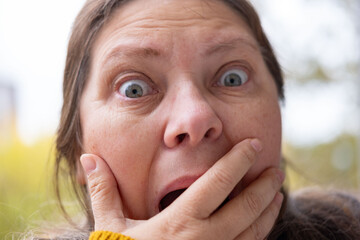 middle-aged mature woman with bulging eyes, face close-up, goggle eyes in fright, startled and...