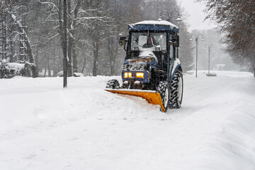 Municipal maintenance in extreme weather: tractor working to clear a wide avenue lined with street lights and trees in deep snow