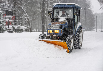 Front view of a snow-clearing tractor working in a public park, overcoming deep snow accumulation during heavy snowfall