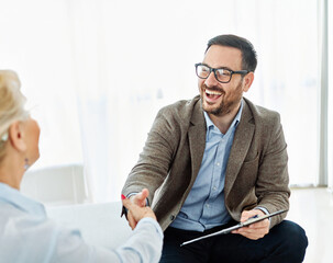 Portrait of a businessman or real estate agent or doctor shaking hands and signing a deal contract with senior woman or businesswoman in his office