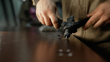 Worker hands using rivet gun joining metal parts