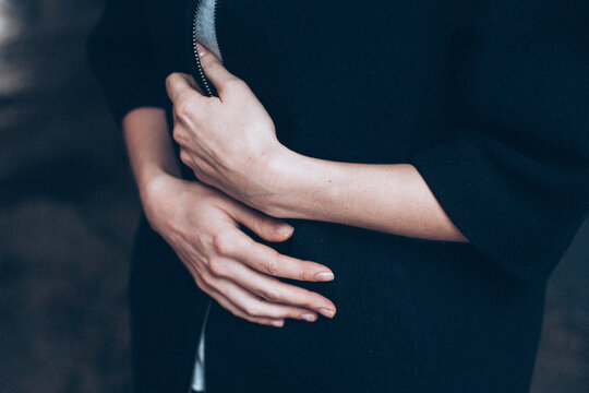 Close-up of a Woman's hands pulling her jacket around her stomach