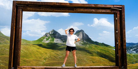 Girl with wooden frame in National park Durmitor, Montenegr. Young woman making photo with beautiful nature landscape and mountains