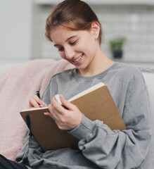 Pretty Girl Sitting On The Sofa At Home Writing Plans And A To-Do List In A Notebook