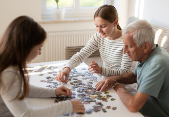 Grandpa And Granddaughters Work On A Puzzle Together, Different Generations Of A Family Spending Time Together