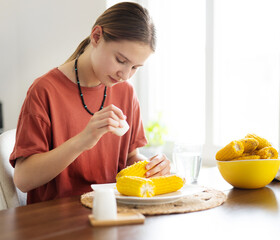 Young Girl Salting Boiling Corn Cobs For Eating In The Kitchen