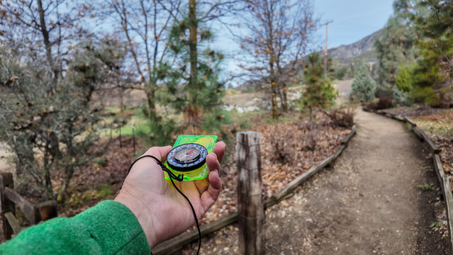 Oak Glen, California, January 6, 2025: A Compass being used on the trail to find direction using the magnetic field of the earth with a needle that points at magnetic north with a bezel to set the dir