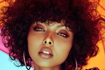 Model with curly hair posing against colorful background in studio setting during daytime