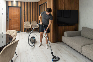 Man vacuuming laminate floor near sofa with vacuum cleaner