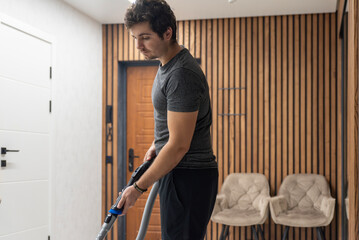 Young man holding vacuum cleaner hose in hallway ready to clean