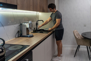 Young man washing dishes at kitchen sink in modern apartment