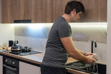 Man washing glass under faucet in modern kitchen at home